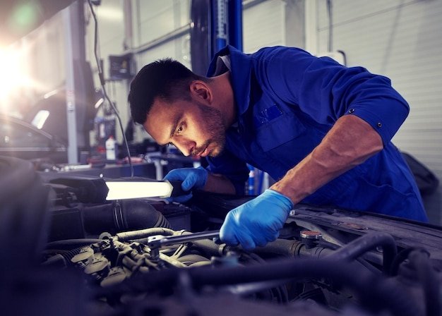 mechanic man with lamp repairing car at workshop