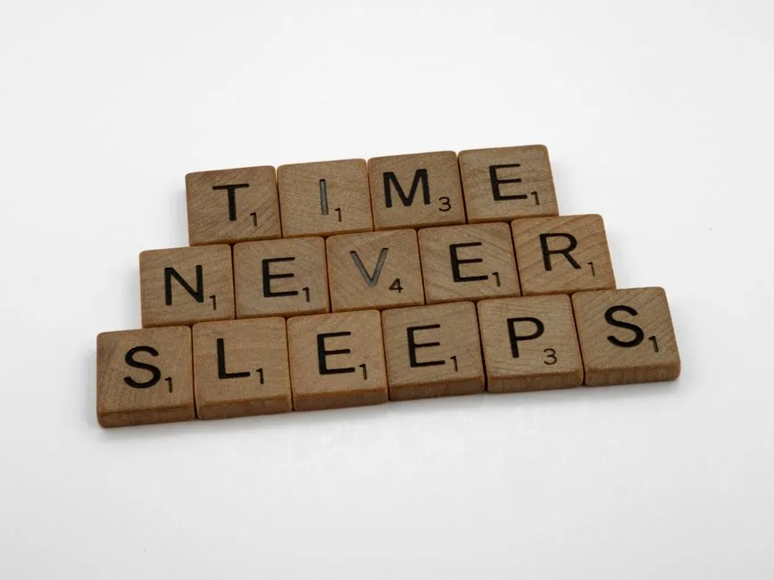 Wooden Scrabble tiles arranged to spell 'Time Never Sleeps' on a white background.