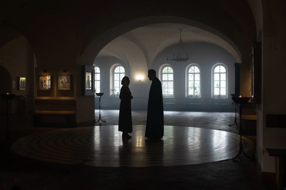 A priest and parishioner silhouetted in a serene church setting.