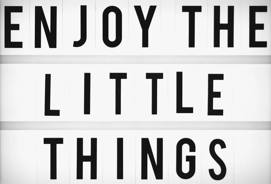 Minimalist design of the inspirational quote 'Enjoy The Little Things' displayed on a lightbox.