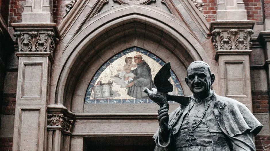 A statue of a pope holding a dove at a historic church entrance with beautiful archway.