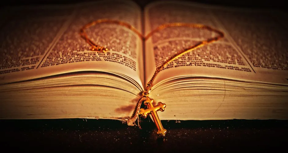 A detailed close-up of an open Bible with a golden cross necklace lying on its pages, creating a spiritual and reflective mood.