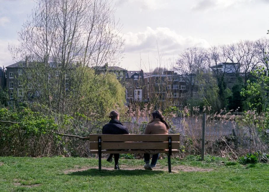 A peaceful scene of two people sitting on a wooden bench in a park.