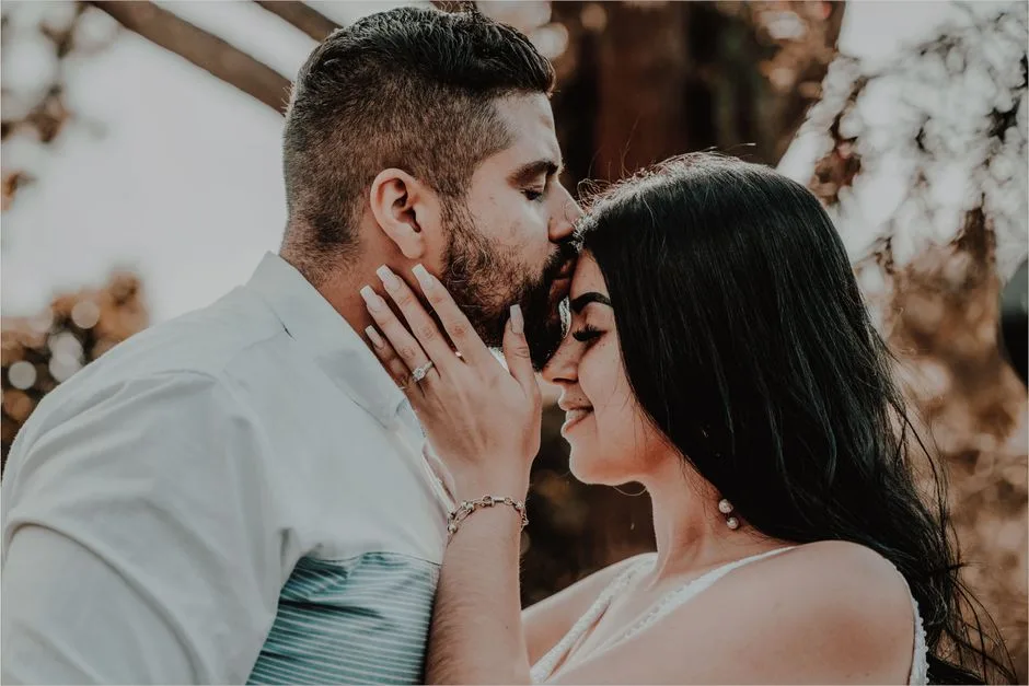 Tender moment of a couple sharing a forehead kiss outdoors, capturing love and serenity.