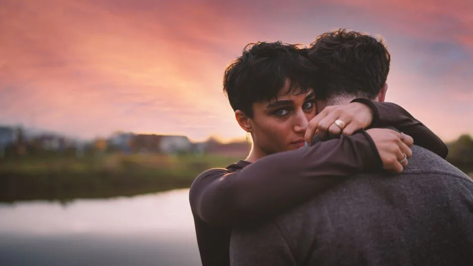 A couple embracing tenderly by the lake during a vibrant sunset, conveying love and warmth.