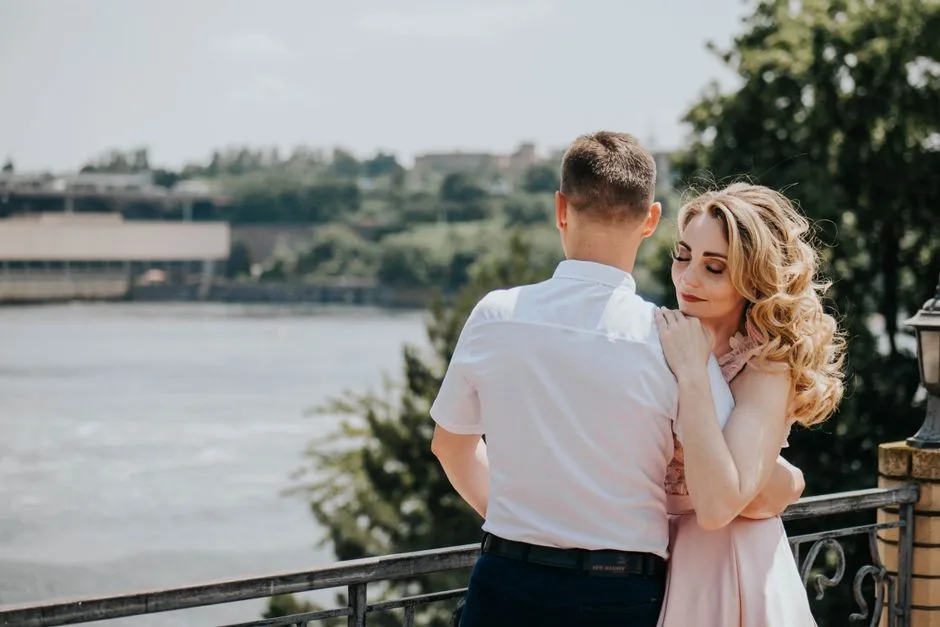 A couple embracing on a balcony overlooking a scenic lake on a sunny day.