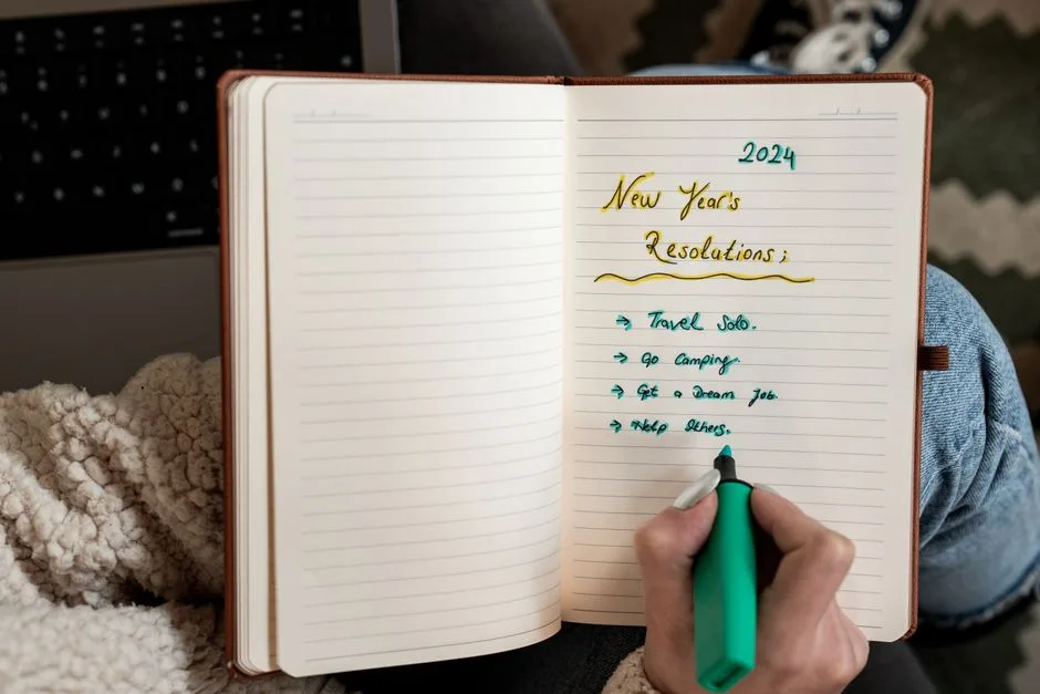 Person making 2024 New Year's resolutions in a notebook with a green marker.
