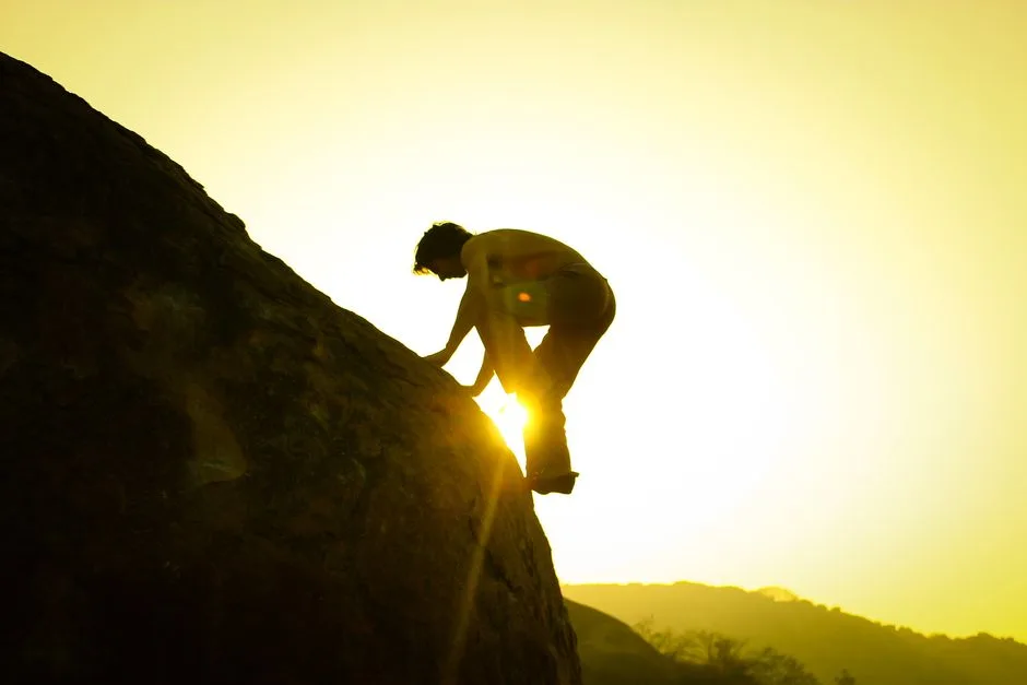 A silhouette of a climber ascending a rock in Hampi, India at sunrise.