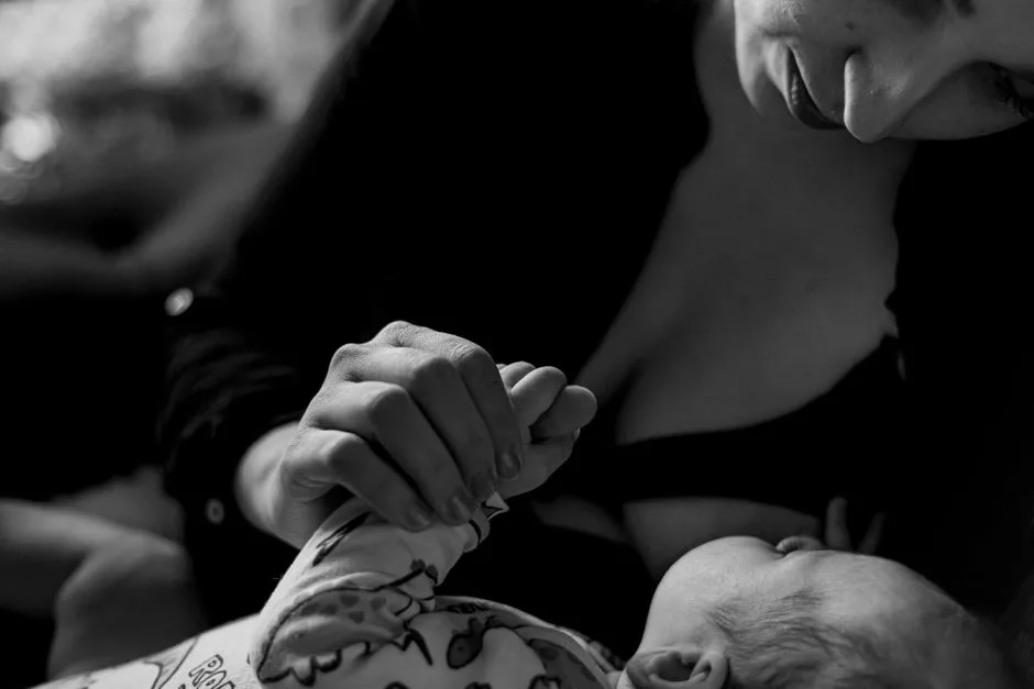 A mother lovingly holds her baby's hand, captured in a touching black-and-white photograph.