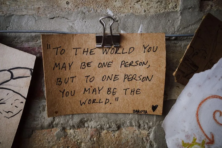 Handwritten inspirational quote on aged paper with a vintage feel, clipped to a textured brick wall.