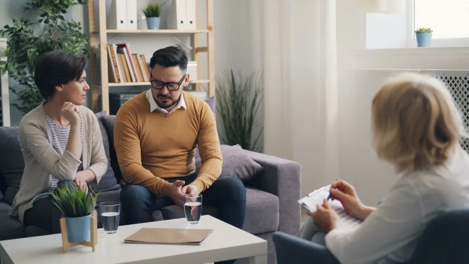 A couple engaged in a counseling session with a therapist in a cozy room.