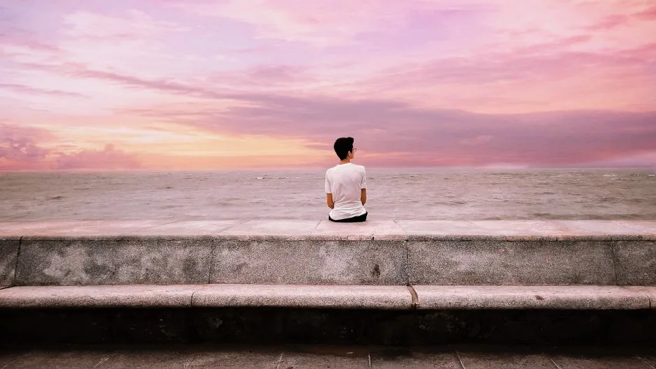 Man sitting alone by the ocean at sunset, embracing peace and tranquility.