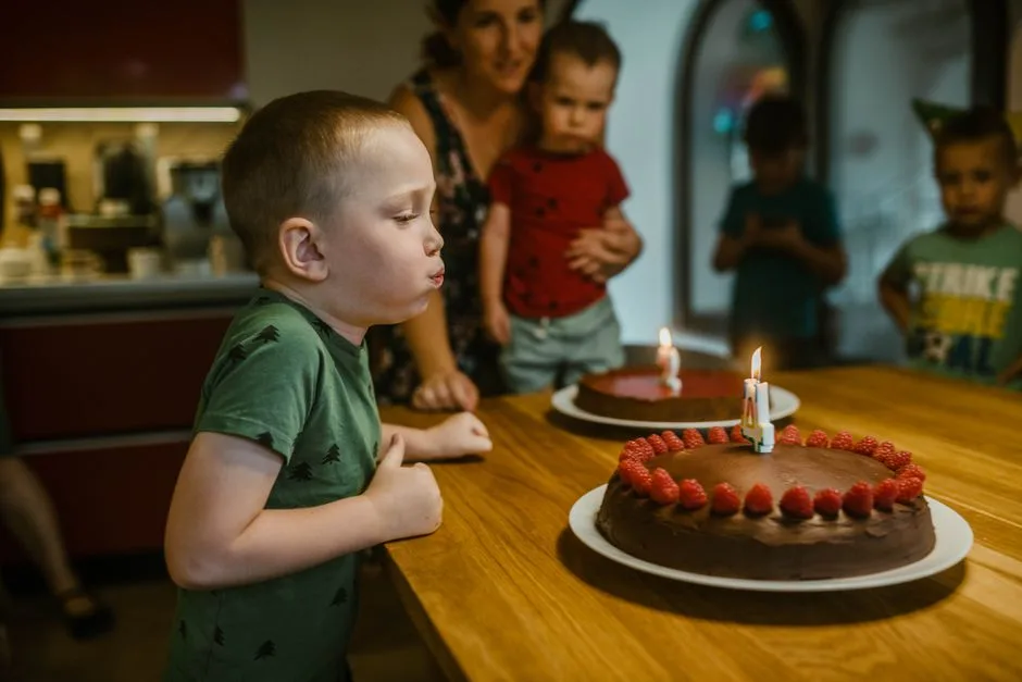 Young boy celebrating birthday by blowing candles on chocolate cake with raspberries.
