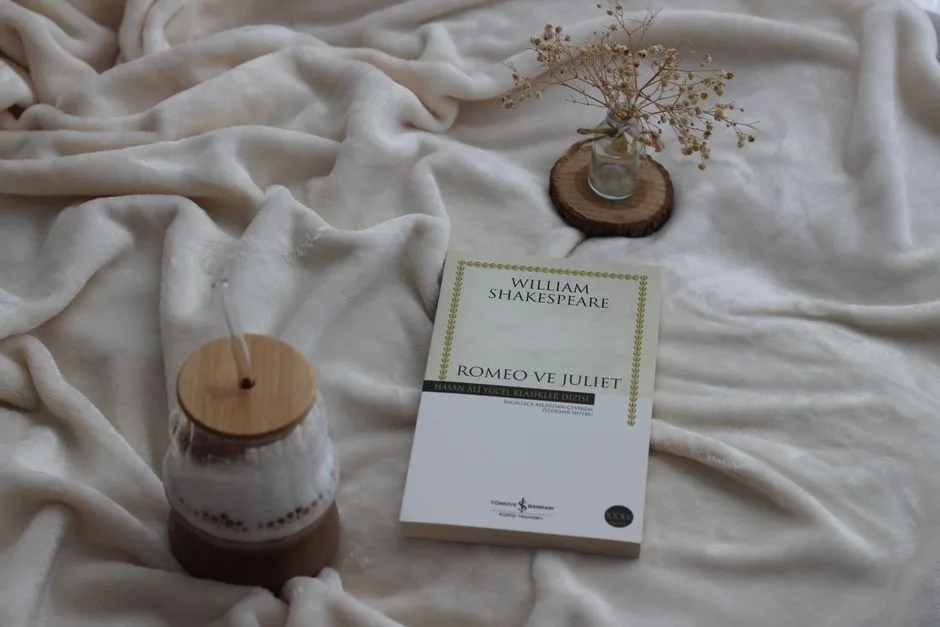 A cozy flat lay featuring 'Romeo and Juliet' on a soft blanket with a candle and dried flowers.