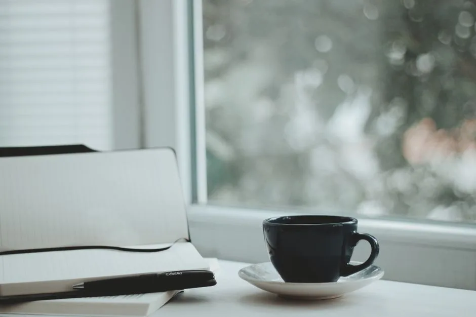 A serene scene with a coffee cup and notebook by a window, perfect for calm mornings.