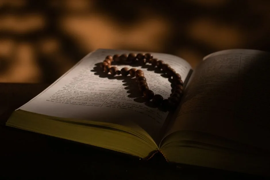 A serene image of an open book with rosary beads, casting soft shadows.