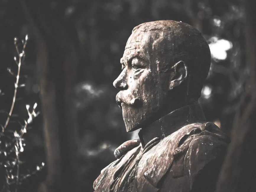 A dramatic monochrome photo of a bust sculpture outdoors, highlighting its weathered texture.