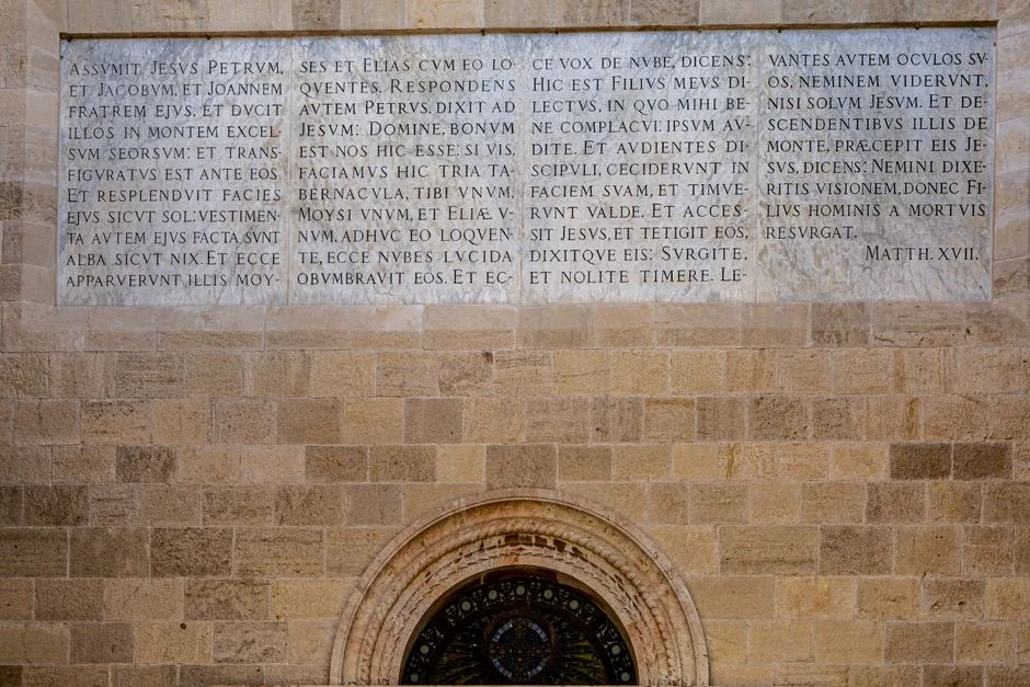 Close-up of a historic wall with Latin script above a circular window.
