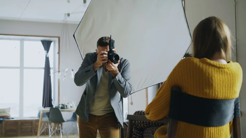 A photographer taking a portrait shot in an indoor studio with natural light.