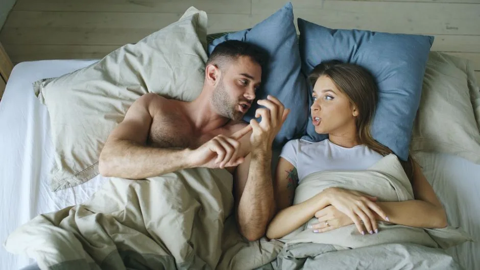 A couple engaged in a casual conversation while relaxing in bed together.