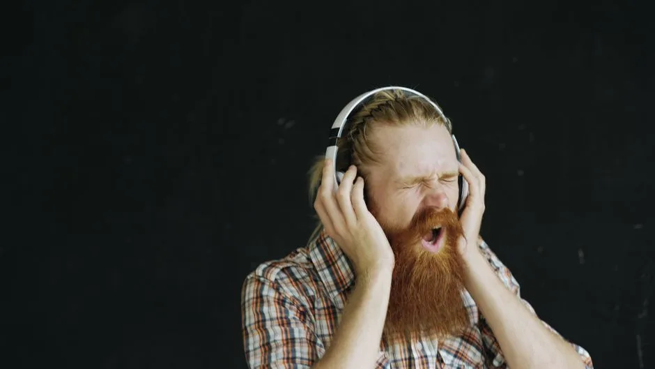 Red-bearded man passionately listening to music with headphones, eyes closed.