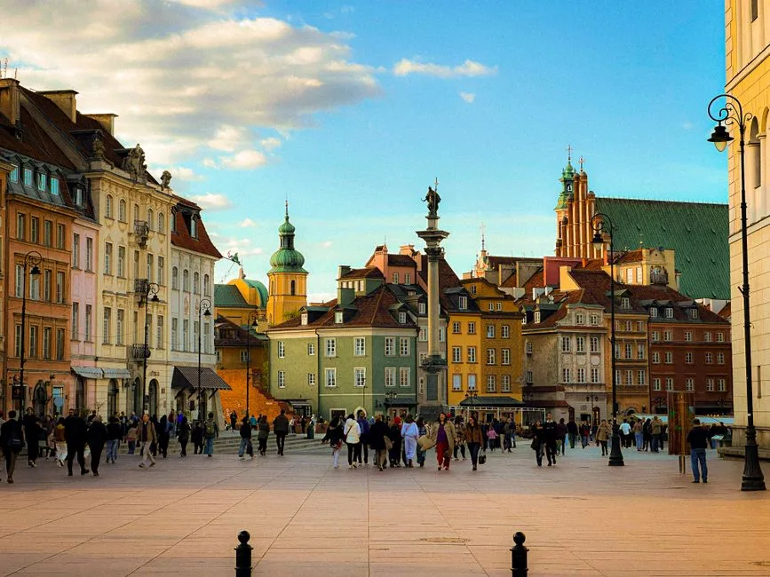 A vibrant view of Warsaw's Old Town Square bustling with people and colorful historic buildings under a clear blue sky.