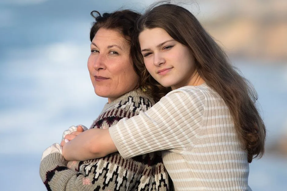 A mother and daughter share a warm embrace at the beach, depicting familial love and connection.