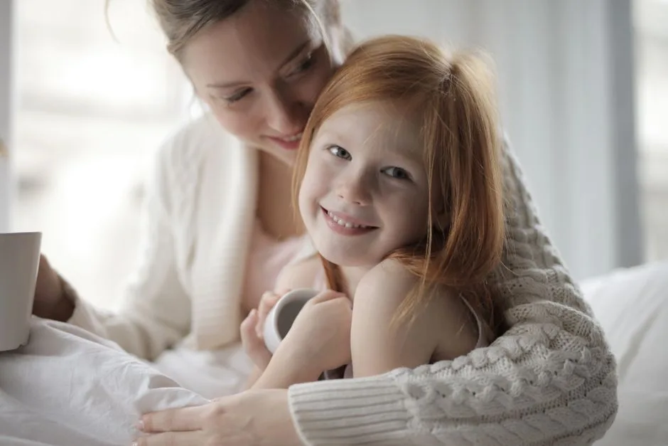 Warm indoor portrait of a mother embracing her young daughter, sharing a cozy moment.