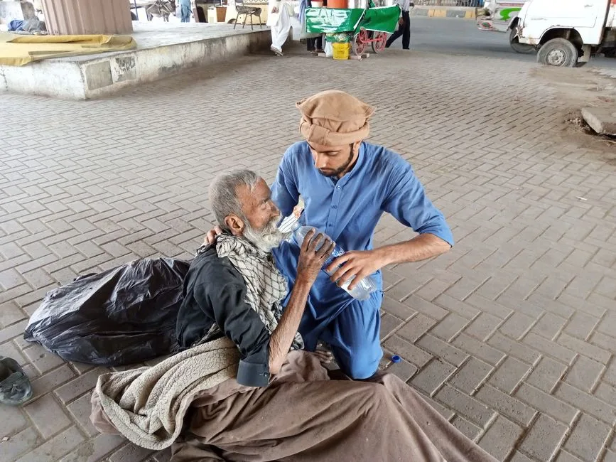 A man providing water to an elderly person on a street in Karachi, Pakistan, highlighting compassion and aid.