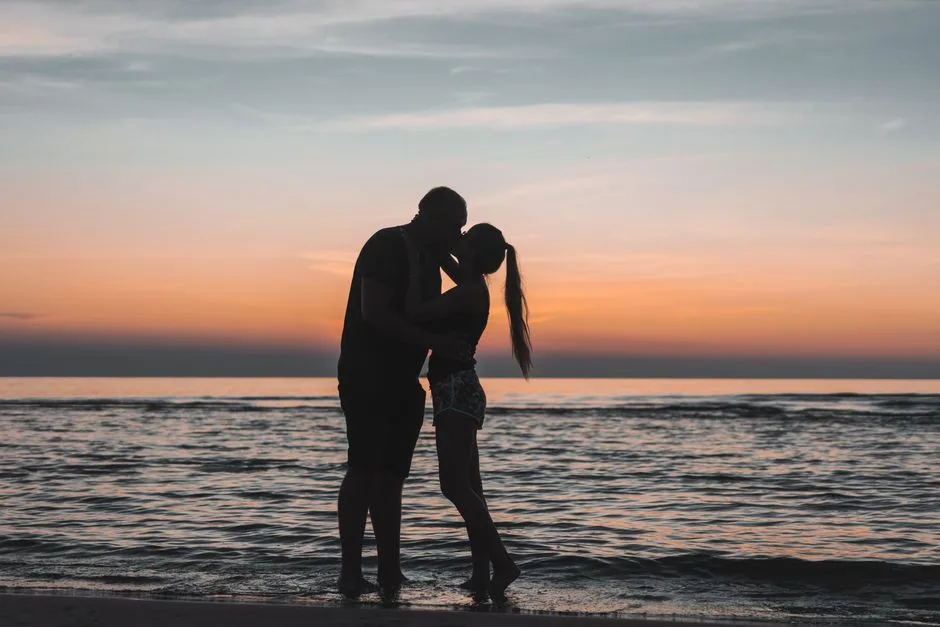 Silhouette of a couple sharing a romantic kiss at a serene beach sunset.