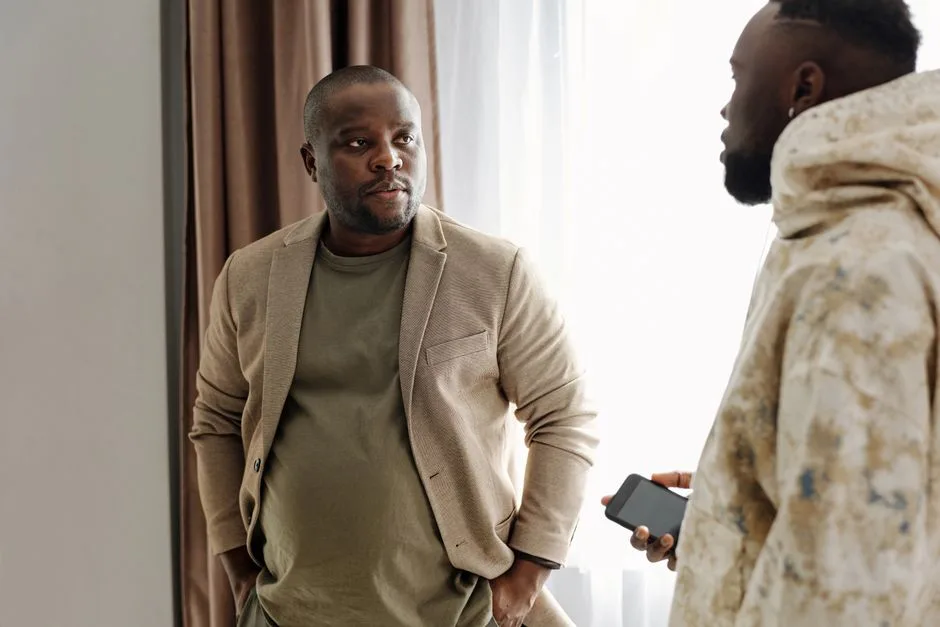 Two men engaged in a serious conversation indoors, one holding a smartphone.