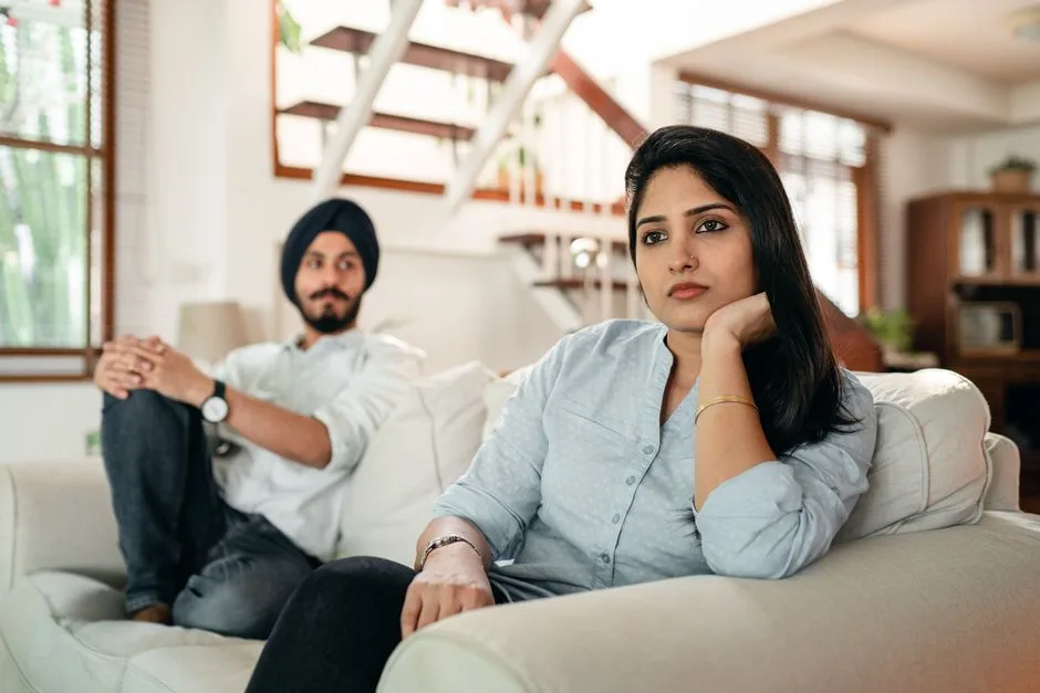 Sad pensive young Indian woman in casual wear sitting on sofa and looking away after quarreling with husband