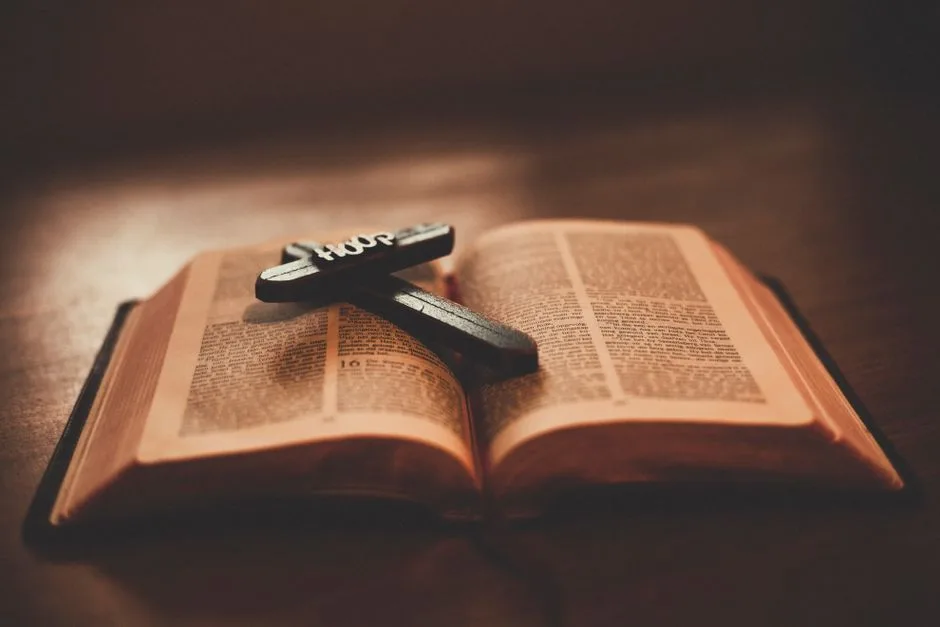 Close-up of an open Bible with a wooden cross inscribed with 'Hope' on a table.