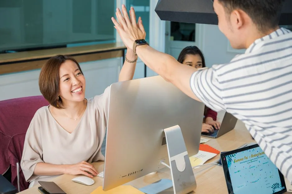 Group of professionals celebrating with a high five at their office desk, promoting teamwork and cooperation.