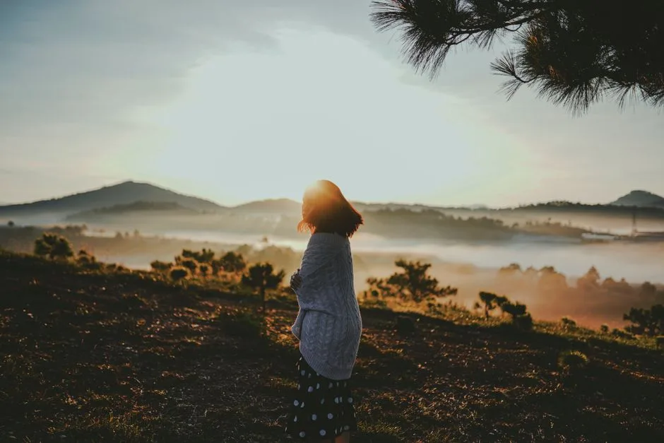 Woman in Dalat, Vietnam enjoying a peaceful sunrise with misty mountain landscape.