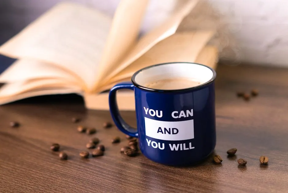 Inspirational coffee moment with a motivational quote on a mug beside an open book.