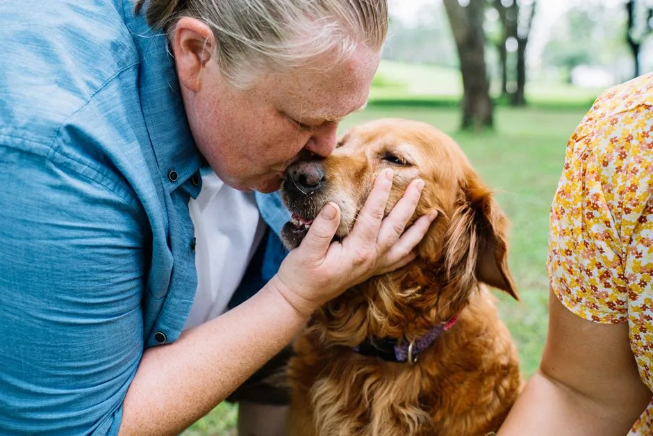 A heartfelt moment of a man kissing his golden retriever outdoors, showcasing love and companionship.