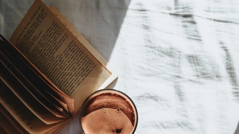 A warm morning scene with coffee and an open vintage book on white sheets.