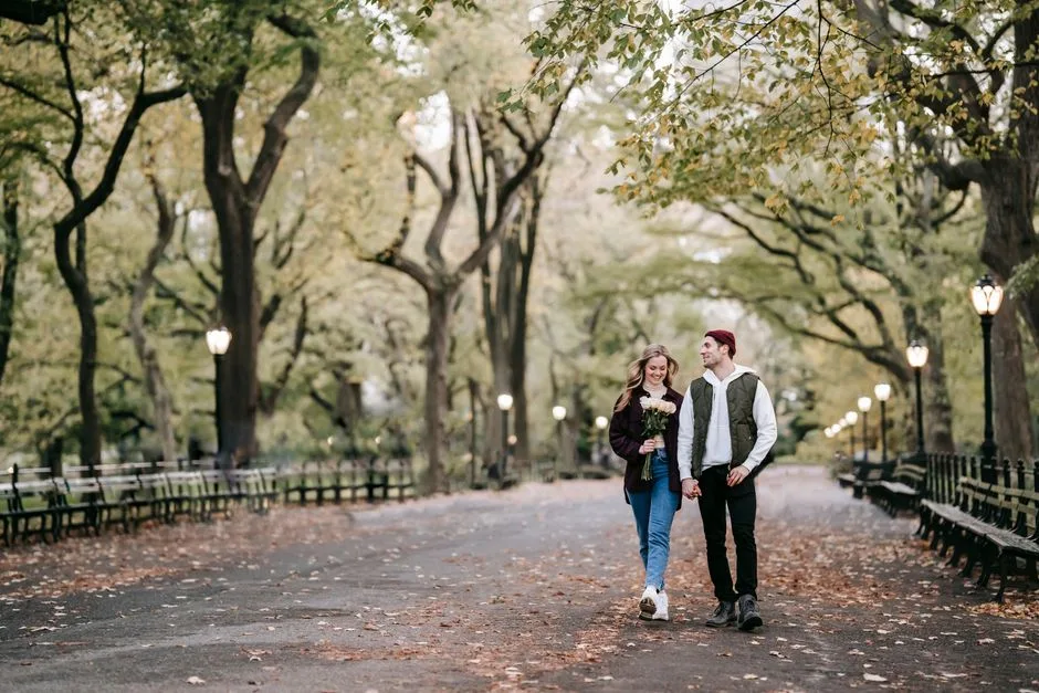 Full body loving couple strolling along autumn park with flowers and holding hands