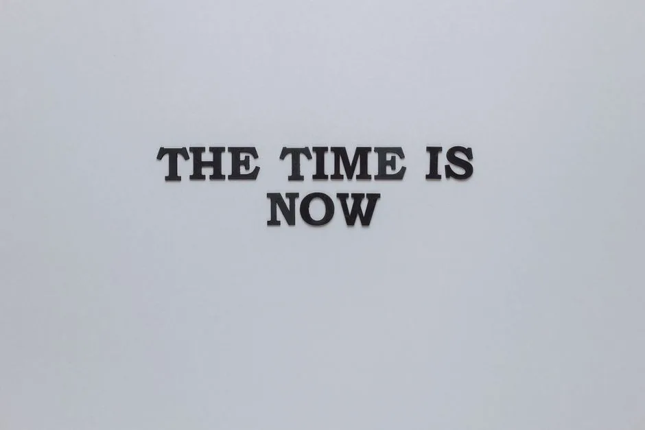 Minimalist poster with the motivational quote 'The Time is Now' on a gray background.
