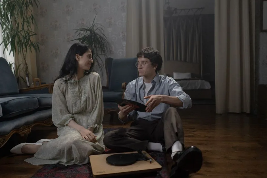 A couple sitting on the floor sharing a vinyl record, creating a retro atmosphere in a cozy indoor setting.
