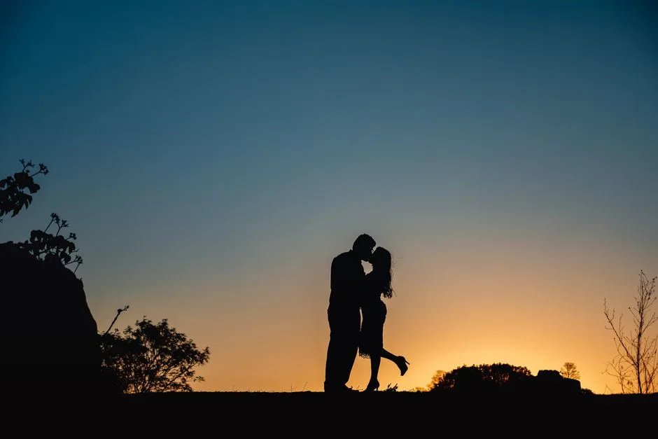 Silhouette of a couple kissing outdoors at sunset, capturing a moment of romance and love.