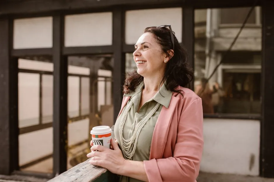 Mature woman happily holding coffee outdoors in an urban setting.