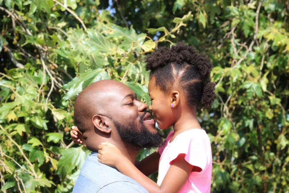 A loving father and daughter share a joyful embrace in a sunny outdoor setting.