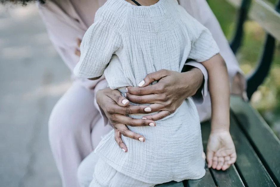 A warm, affectionate hug between mother and child sitting outdoors on a wooden bench.