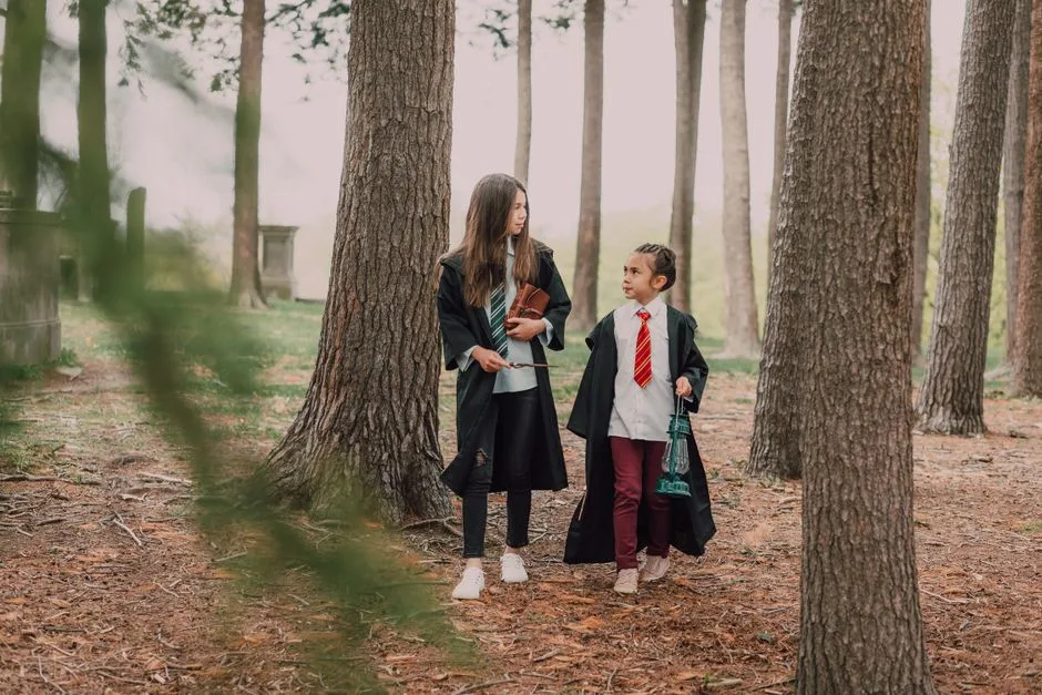 Two children in wizard outfits wandering through a magical forest with wands and robes.
