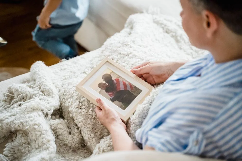 A woman wrapped in a blanket holds a framed family photo while relaxing on a couch.