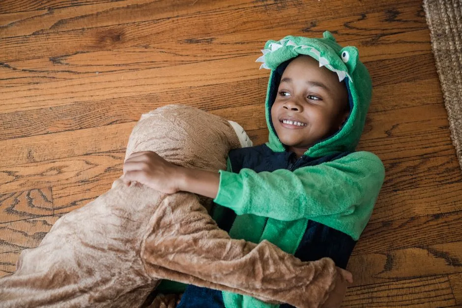 Two children in costume sharing a joyful hug on wooden floor indoors.