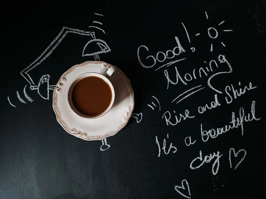 Cup of coffee on chalkboard with a cheerful good morning message and illustrations.