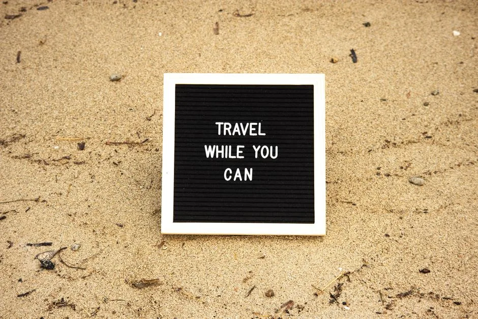 Quote 'Travel While You Can' on board in sand, inspiring travel and adventure.